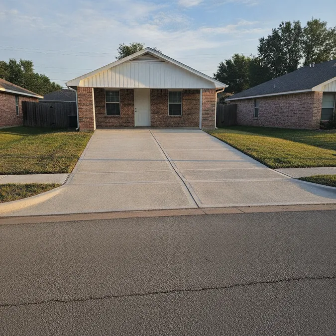 A finished replacement driveway has a broom surface, planned joints, and a clean garage transition.